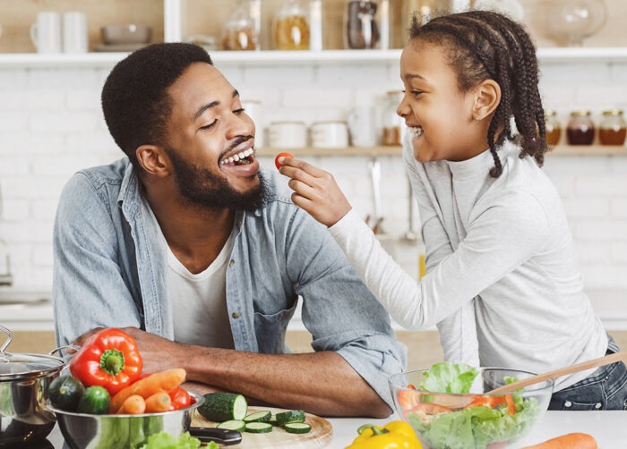 daughter feeding her father tomatoes in the kitchen